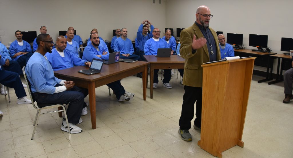 man speaking at podium with incarcerated behind him