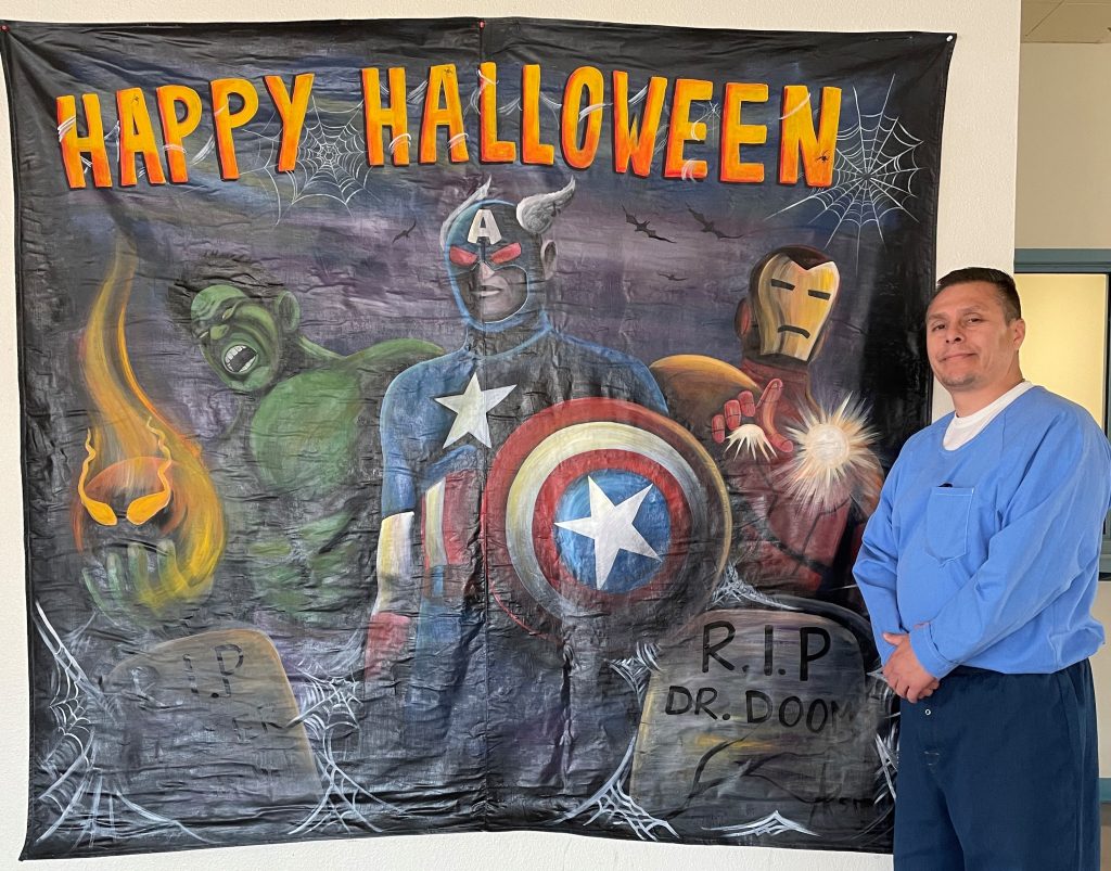 A happy Halloween photo backdrop painting and the incarcerated artist at the California state prison in Tehachapi.