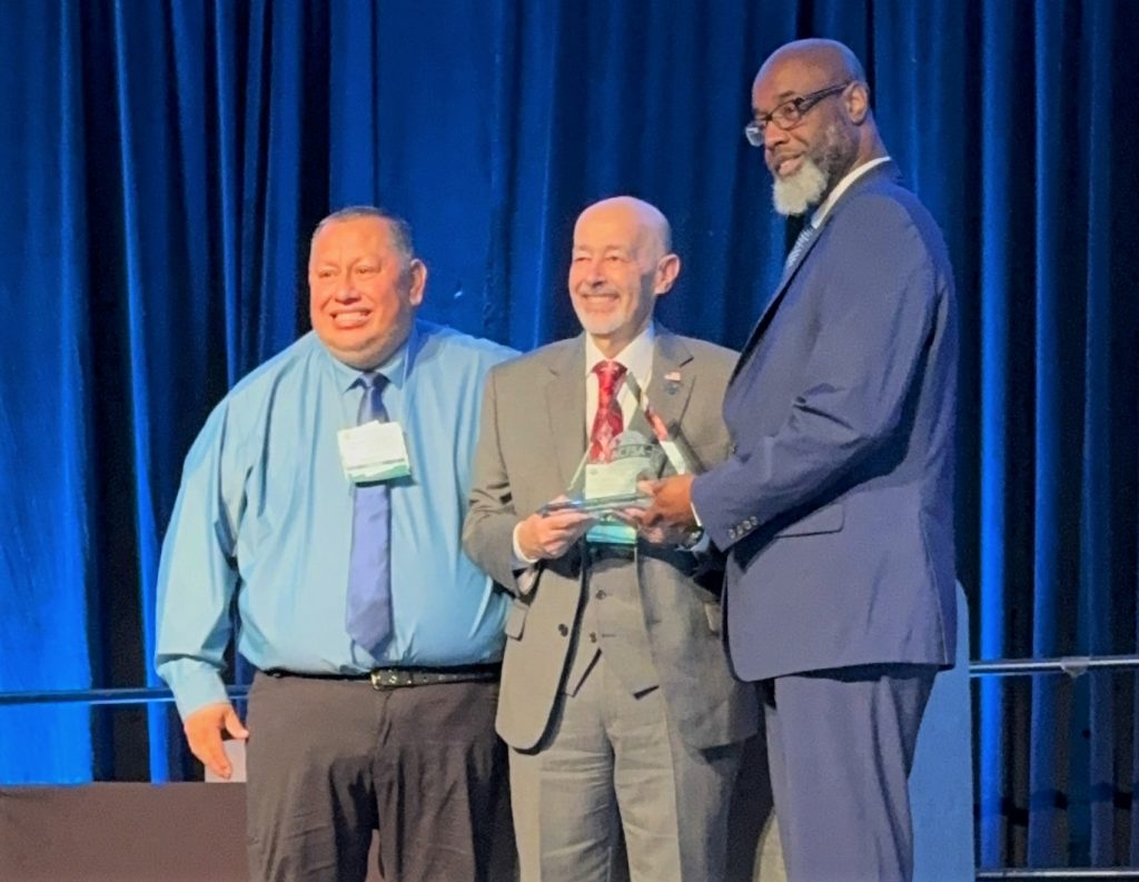 Philip holding award with two gentlemen