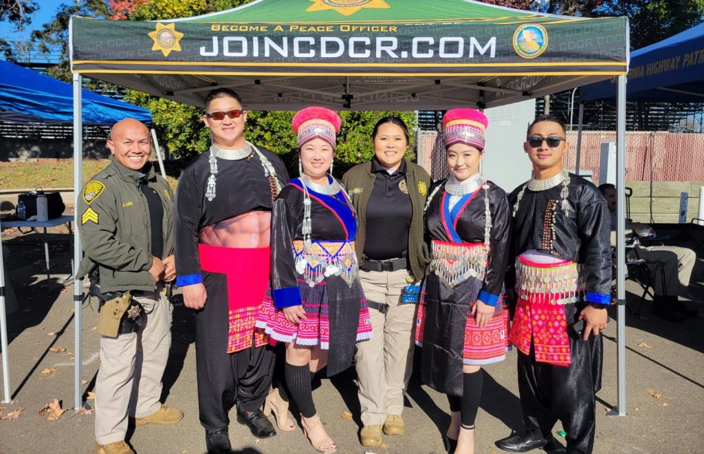 Two recruiters with four people in traditional outfits at the Hmong New Year celebration at Cal Expo in Sacramento.