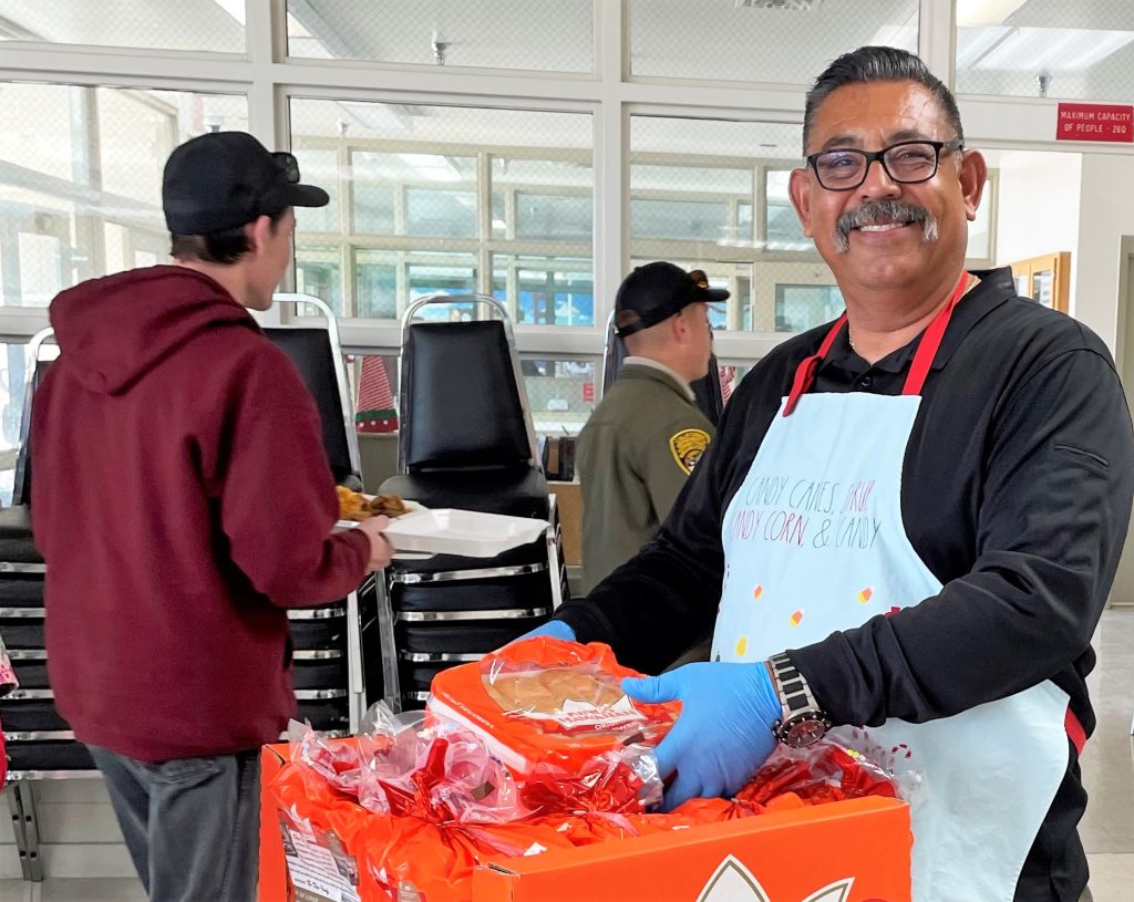 Staff appreciation holidays luncheon at Ironwood State Prison with a man smiling while handing out rolls. 