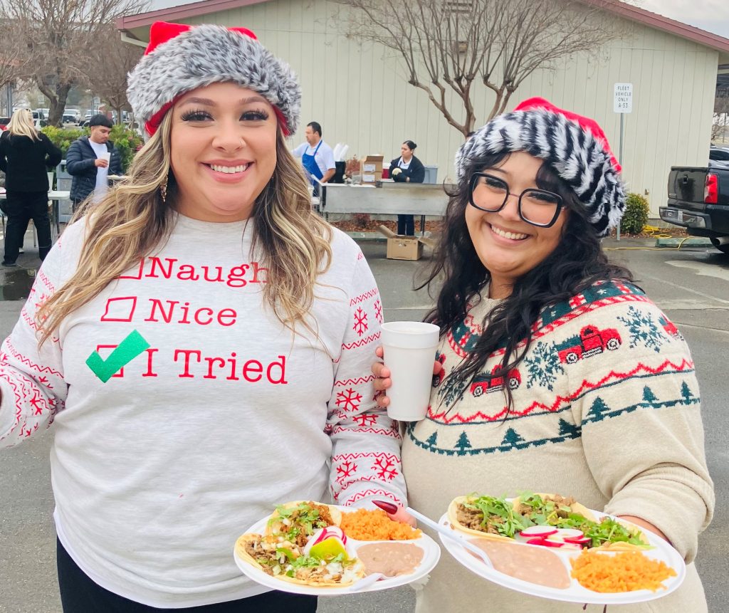 Plates of food and two people wearing Christmas attire attend Pleasant Valley State Prison health care staff holiday lunch.