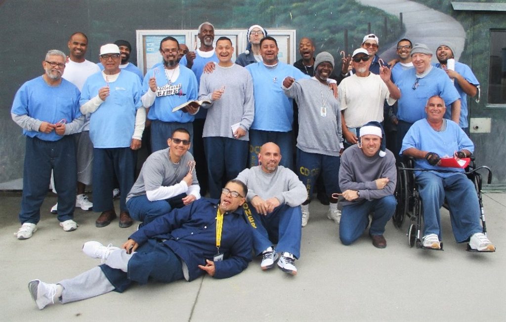 Group photo of incarcerated people and volunteers at RJ Donovan Correctional Facility holding candy canes.
