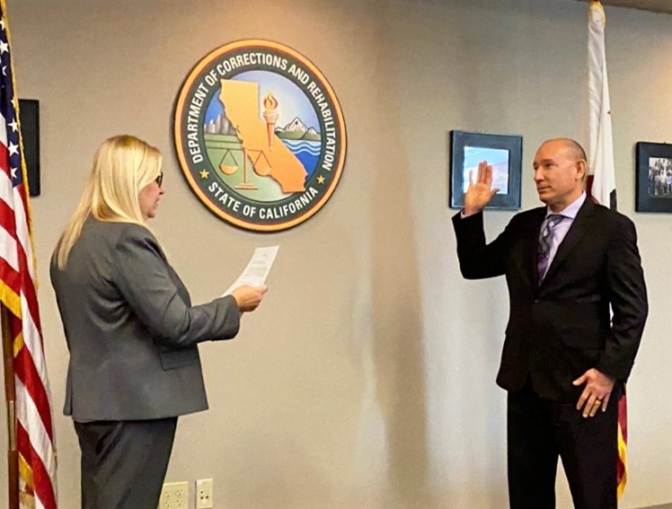 Man raises right hand while being sworn in as warden of Mule Creek State Prison.