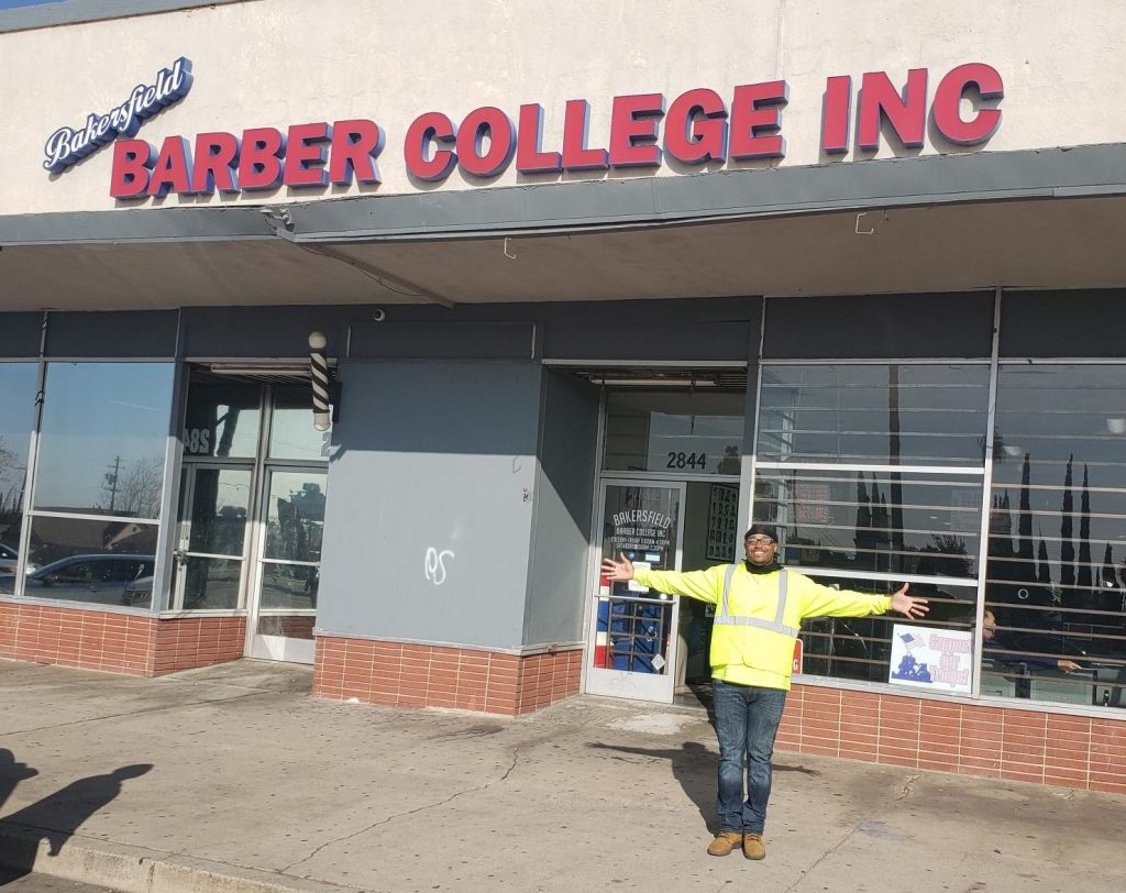A person stands in front of a barber shop.