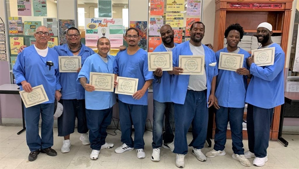 Eight people hold award certificates from an OCE essay writing contest at Folsom State Prison.