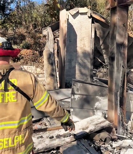 A CDCR fire chief walks through rubble looking for hotspots caused by creosote-treated wood used as foundations for sheds. 