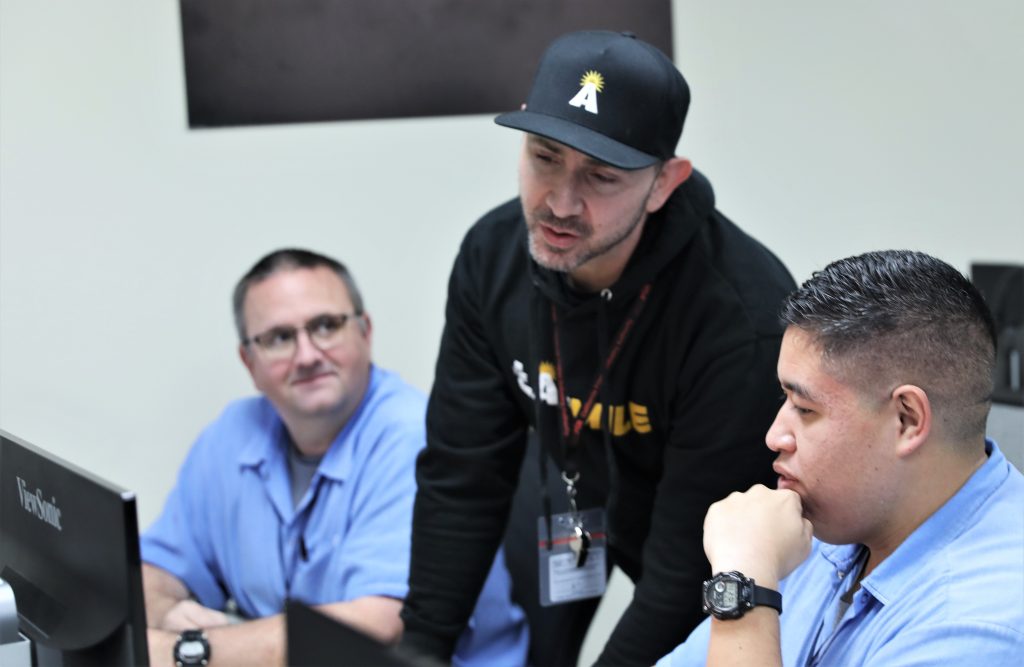 A coding class at San Quentin Rehabilitation Center with a person from the program speaking with two students.