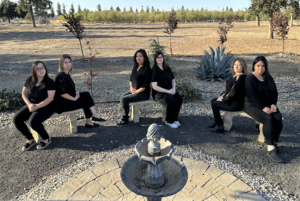 Personnel specialists at Valley State Prison dressed alike to pose for photos to present to their supervisor at Valley State Prison for Boss's Day. The six women are wearing all black outfits and sitting around a fountain.