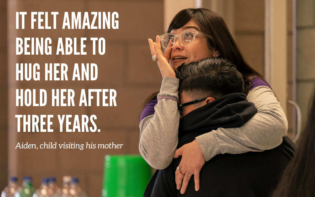 An incarcerated mother hugs her child at CCWF for Camp Grace. Overlaying the image is this quote from Aiden, a child: "It felt amazing being able to hug her and hold her after three years."