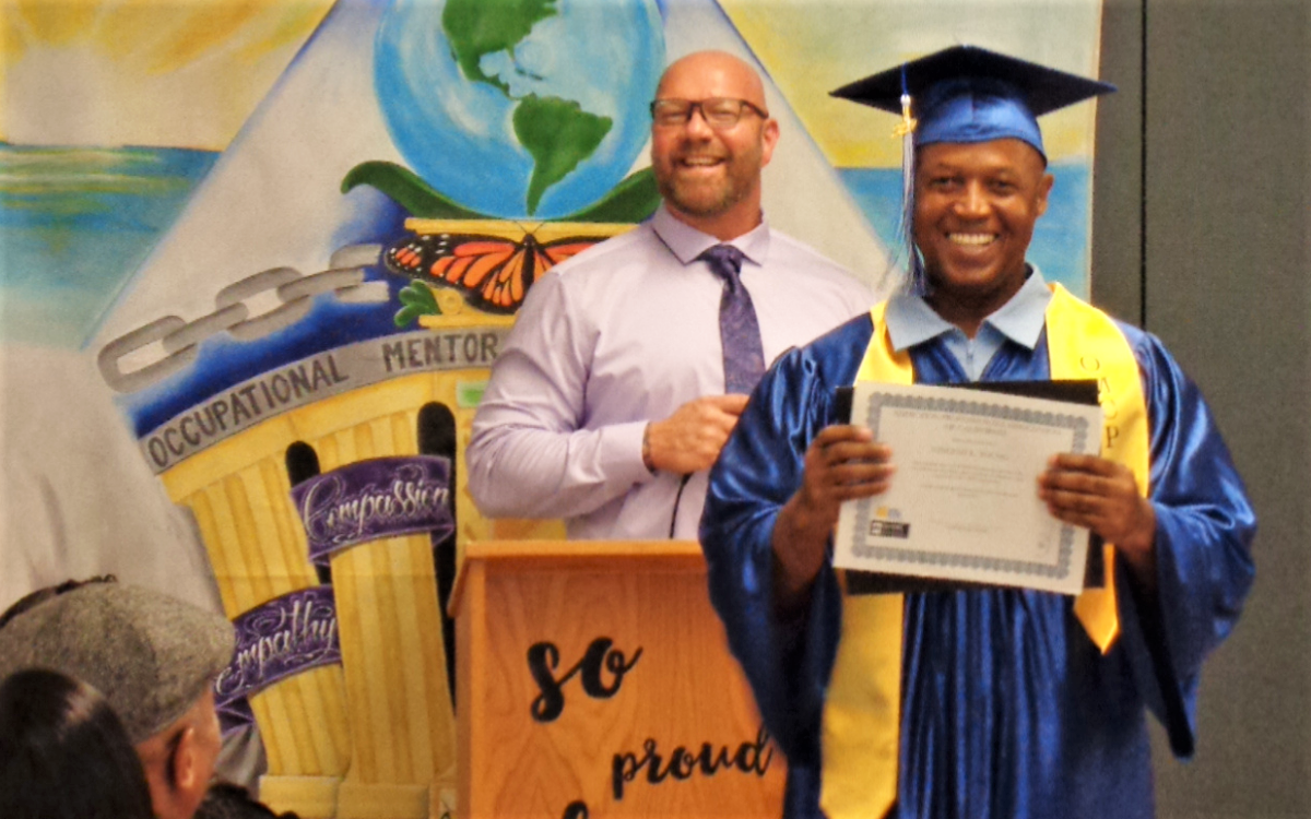 An incarcerated person holds an OMCP certificate at his graduation at Corcoran prison.