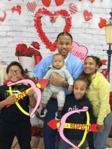 Incarcerated male with four family members pictured in front of a Valentine's Day decorated wall 