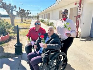 In a courtyard, two staff members present a patient with a rose.