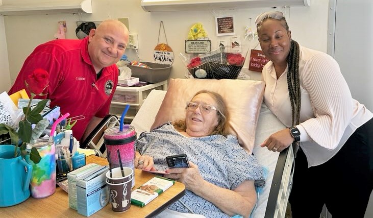 A woman in a nursing home bed is presented Valentine's Day gifts by ISP staff.