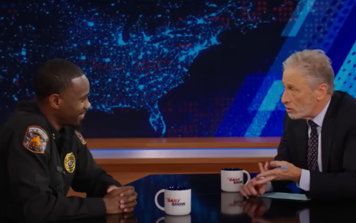 Royal Ramey wears a uniform while sitting across a desk from Jon Stewart on The Daily Show.