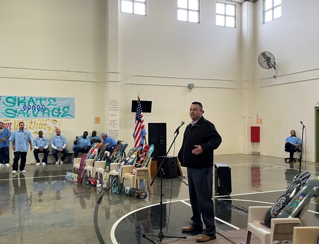Person speaking to a group inside a prison gymnasium.