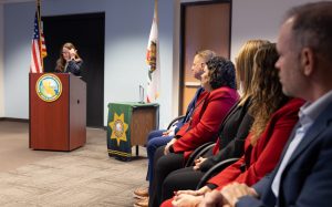 CDCR first Impact Award with someone speaking at a lectern and others seated nearby.