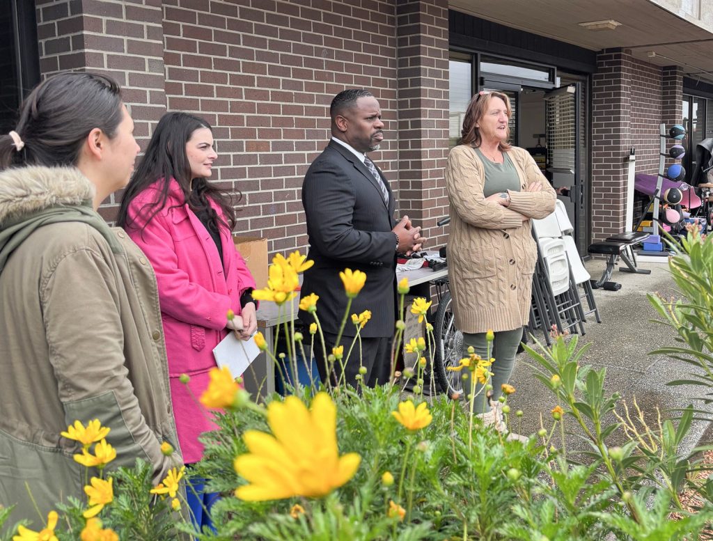 CDCR staff with the director of FCRP-Sacramento on a tour with flowers in the foreground and exercise equipment in the background.
