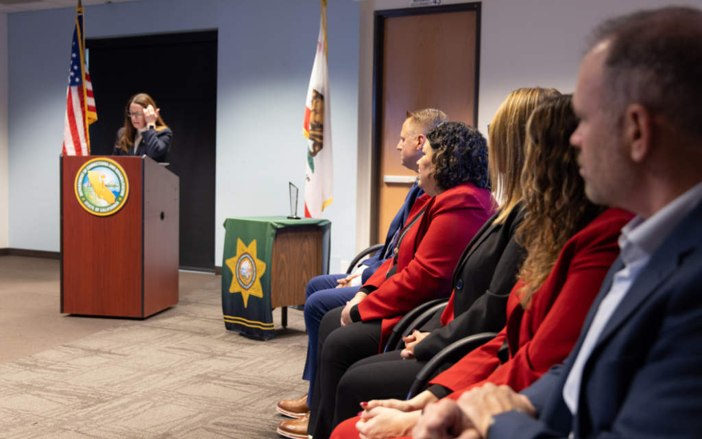 CDCR first Impact Award with someone speaking at a lectern and others seated nearby.