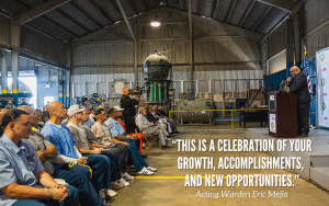 CALPIA dive center graduates with the CIM warden speaking at a lectern.