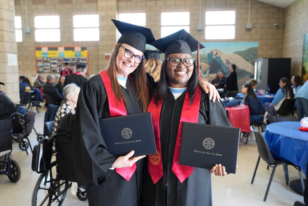 Two women hold their college degrees.