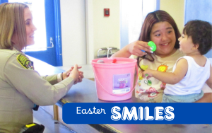CDCR Easter visiting with an officer letting a child choose a plastic egg filled with treats at CSP-Corcoran and the words "Easter Smiles" overlaying the image.