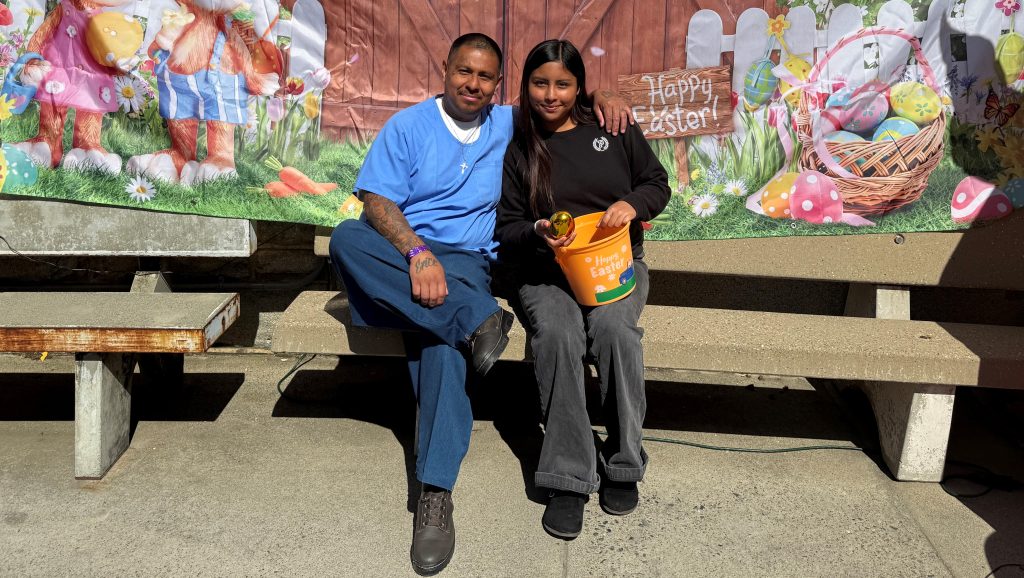 Two people sitting on a bench in front of an Easter photo backdrop.