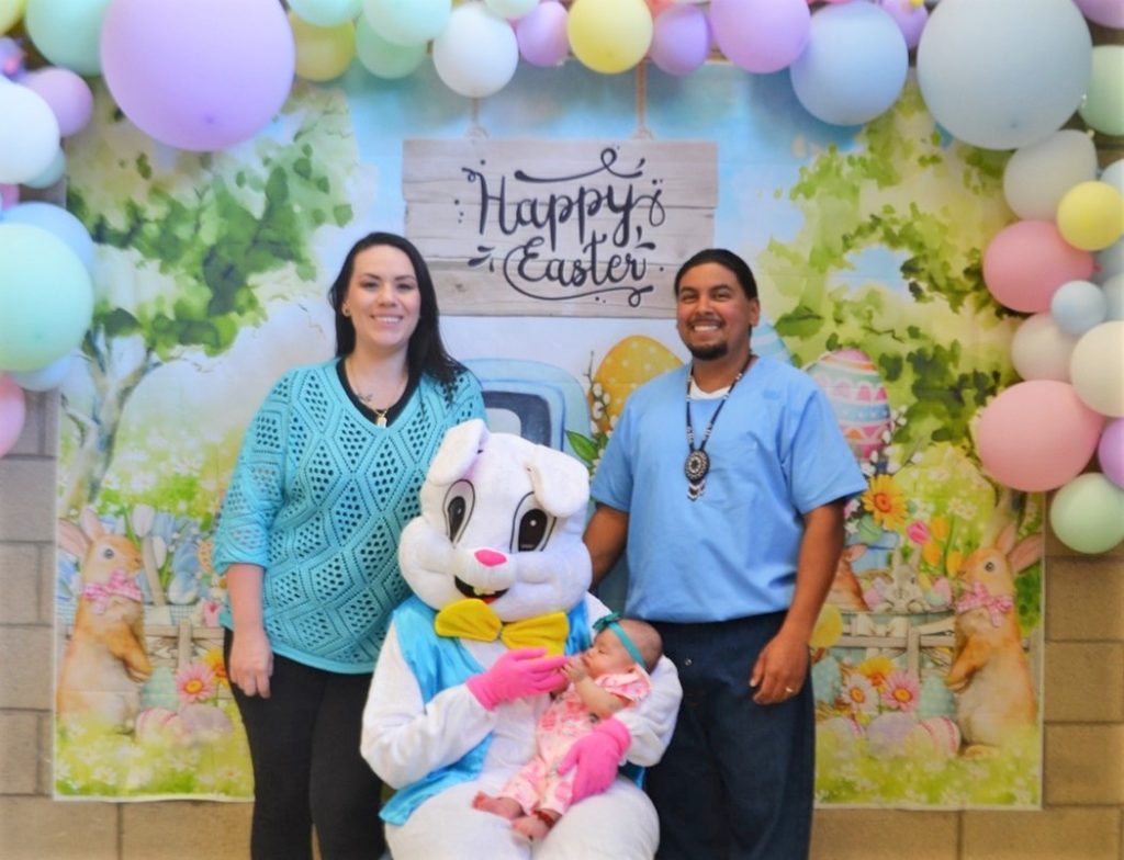 Easter bunny holds baby with two people stand behind.