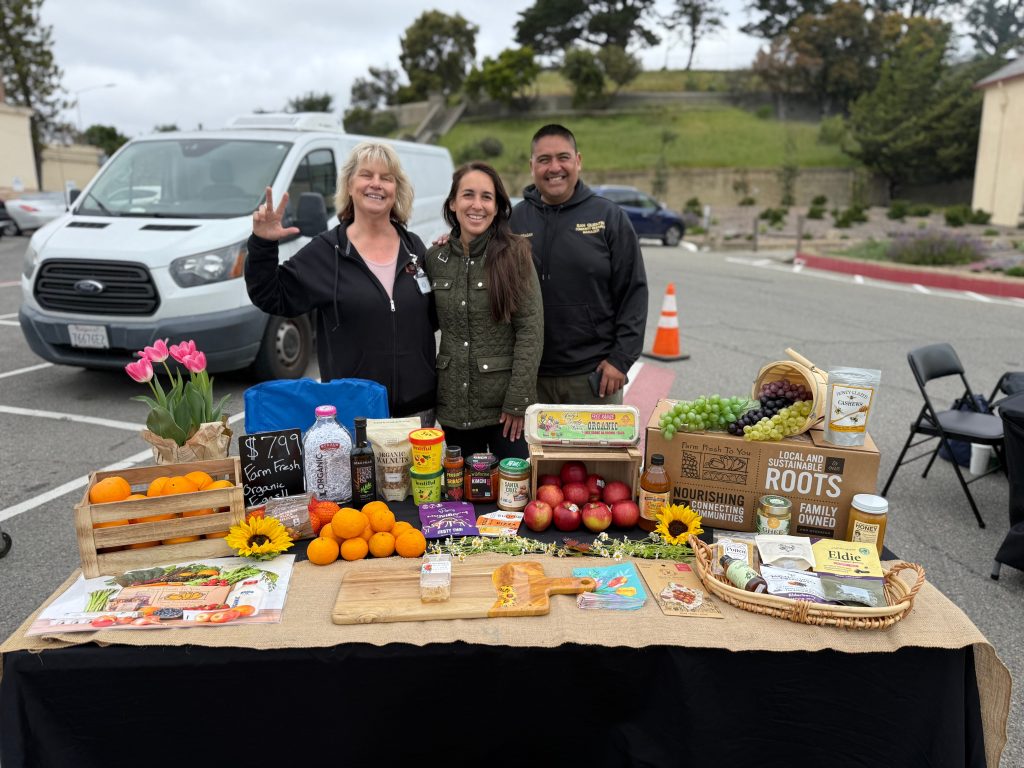 staff smiling behind a table full of healthy fruits and veggies