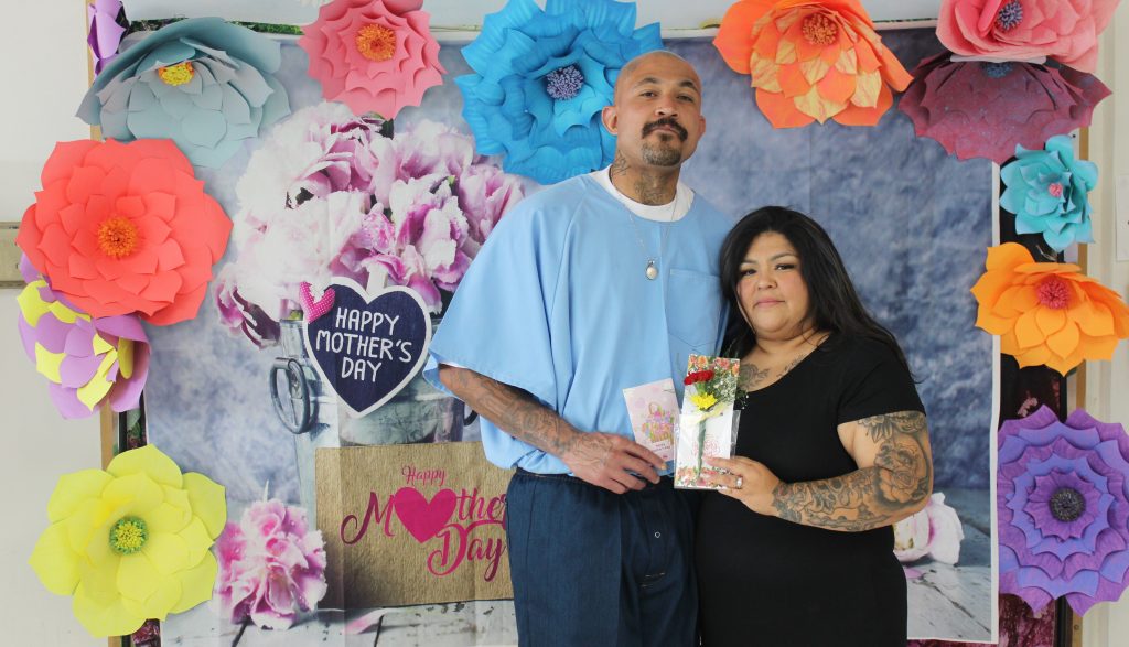 Two people pose for a photo in front of a Mother's Day themed backdrop at Centinela State Prison, Sunday, May 11, 2025.