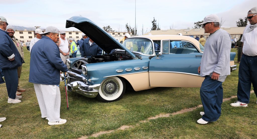 A classic car with the hood up so people can see the engine.
