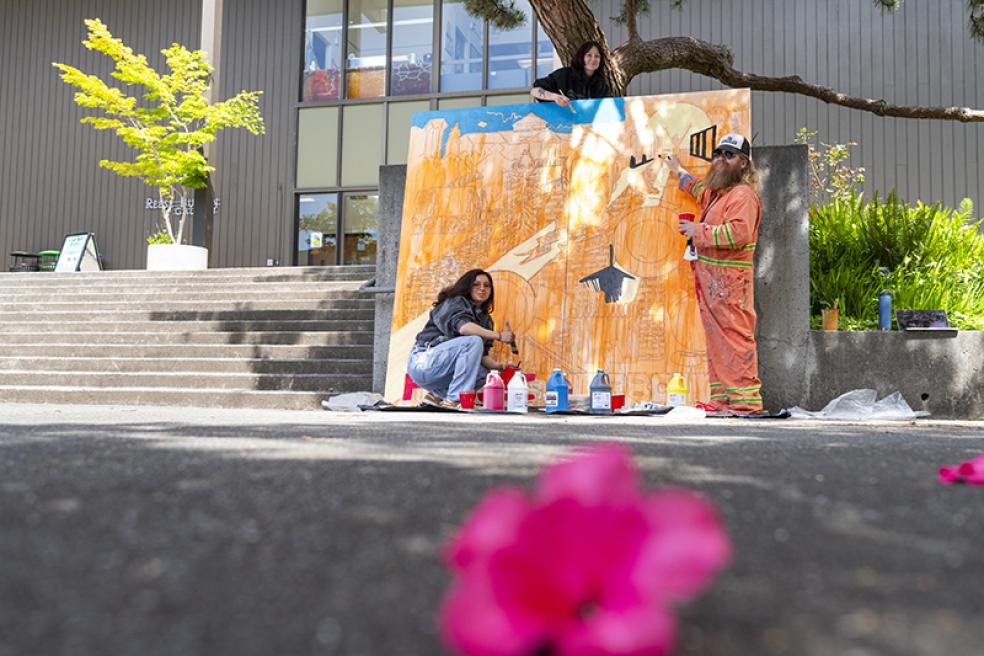 Two students, Alexia Friedman (top) and Mariah Kirkpatrick (bottom), and Art Education Professor James Woglom (right) paint a mural designed by Pelican Bay incarcerated artists.