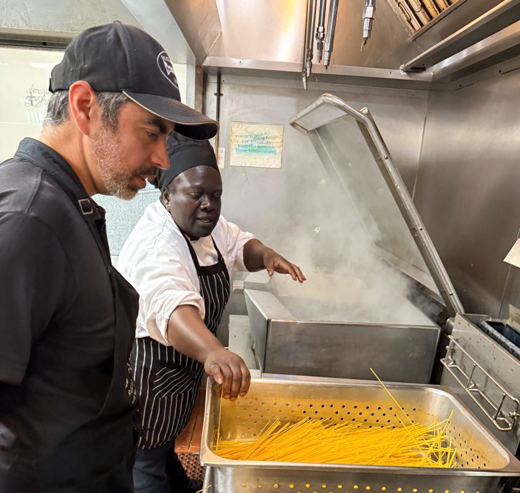 Rescue mission chef prepares pasta while a San Quentin staff member looks on.
