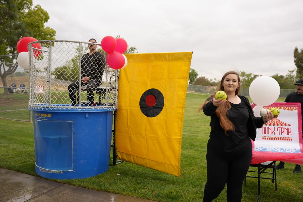 staff posing at the dunk tank, offering a ball