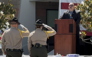 CIM staff salute the flag while Warden Mejia is at the lectern.