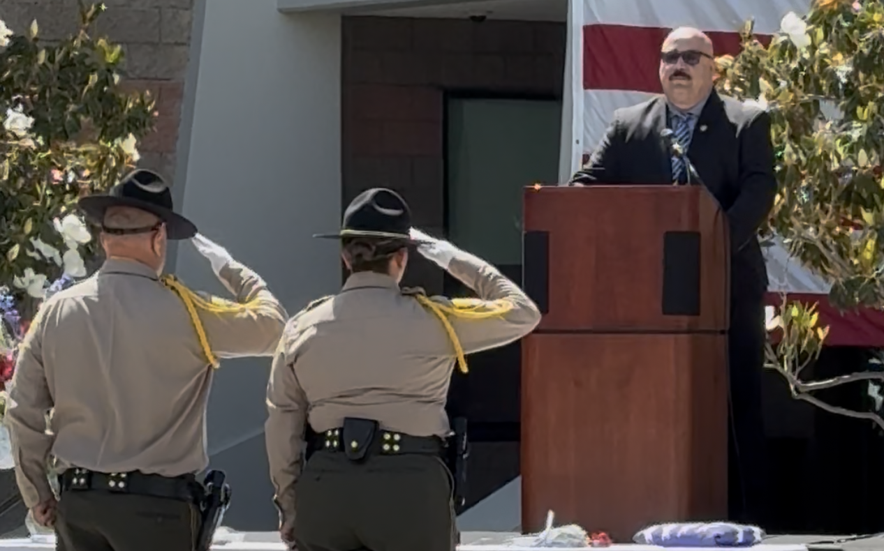 CIM staff salute the flag while Warden Mejia is at the lectern.
