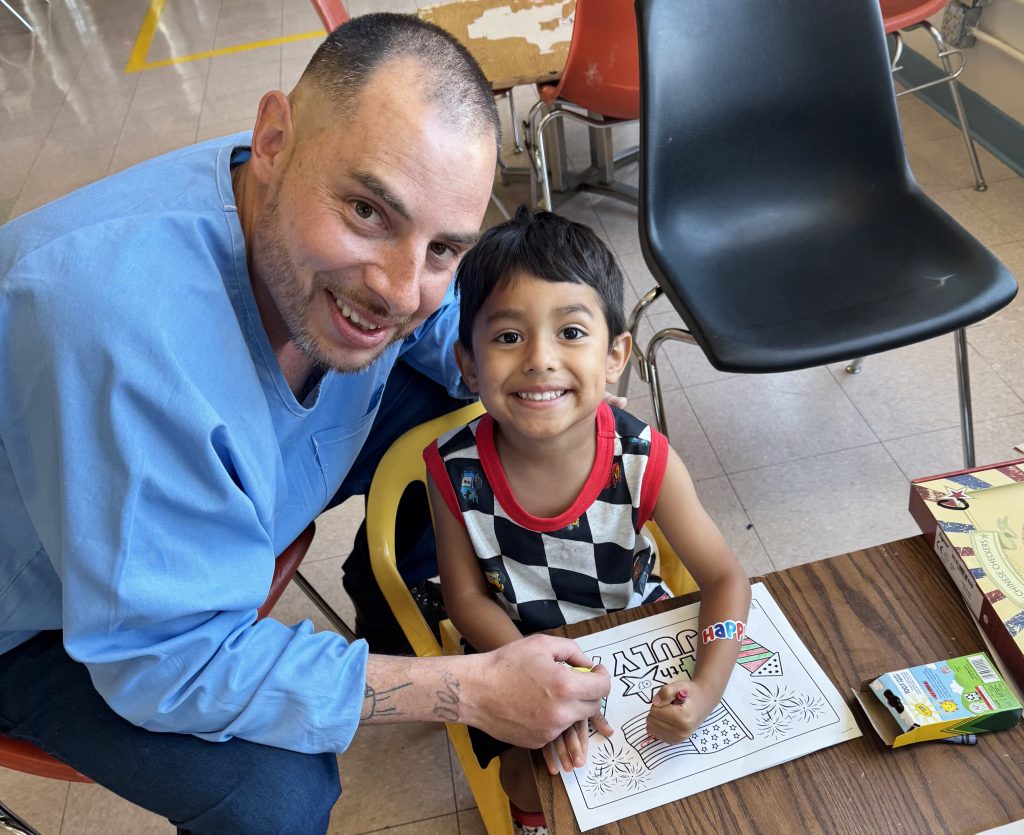 Incarcerated person helps a child with Fourth of July coloring during a visiting event at California Correctional Institution.