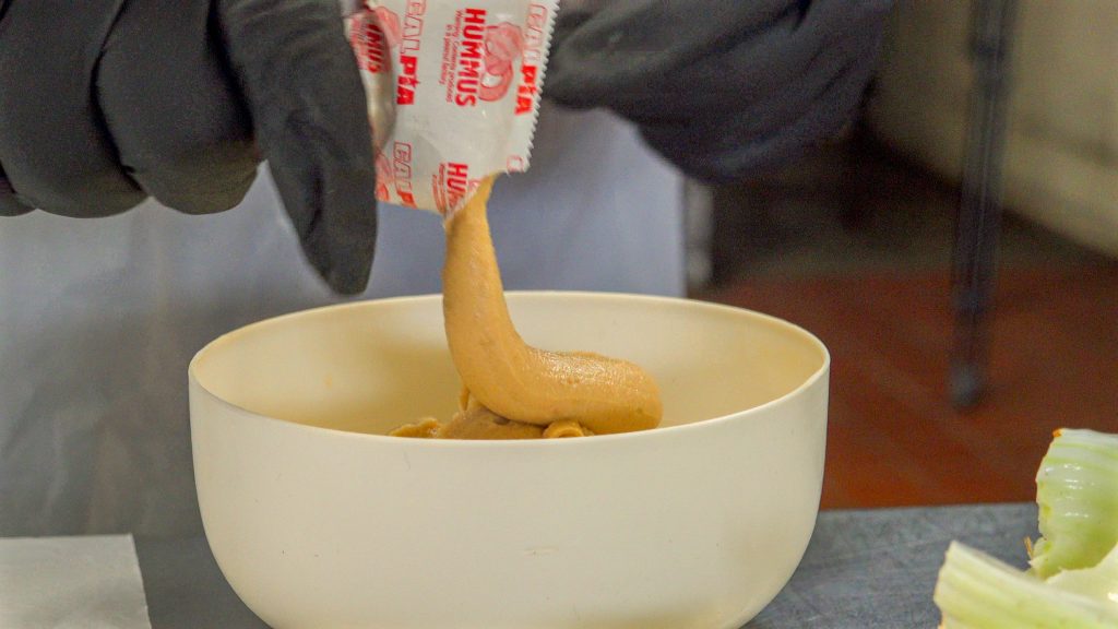 Hummus being squeezed from its package into a bowl.