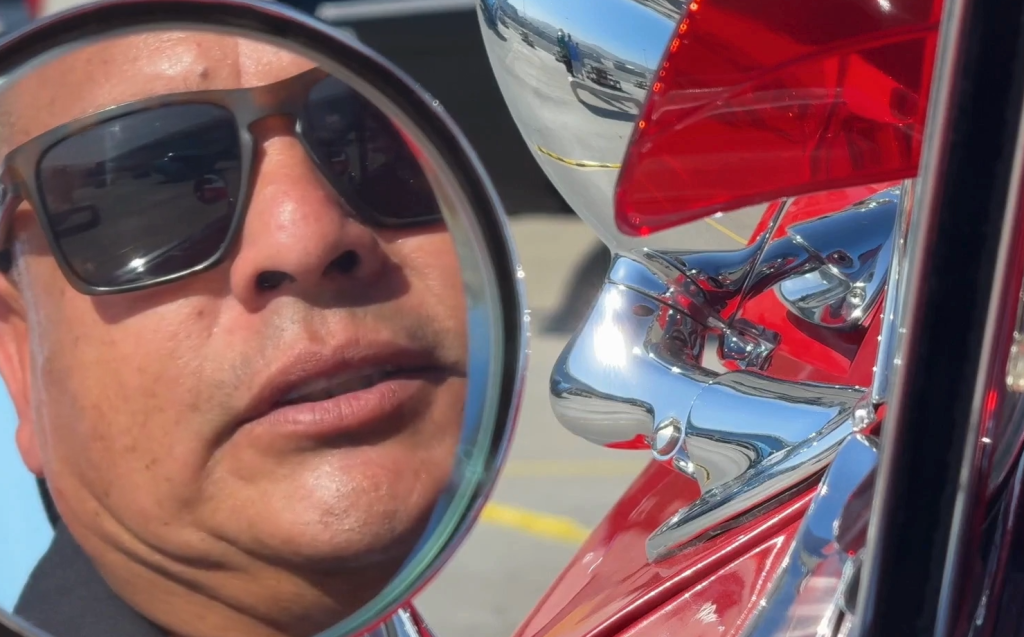 Side mirror reflection of a person sitting inside a lowrider.