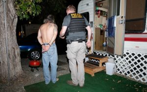 Operation Boo 2018 with man in handcuffs while standing beside a parole agent during a Halloween compliance check.