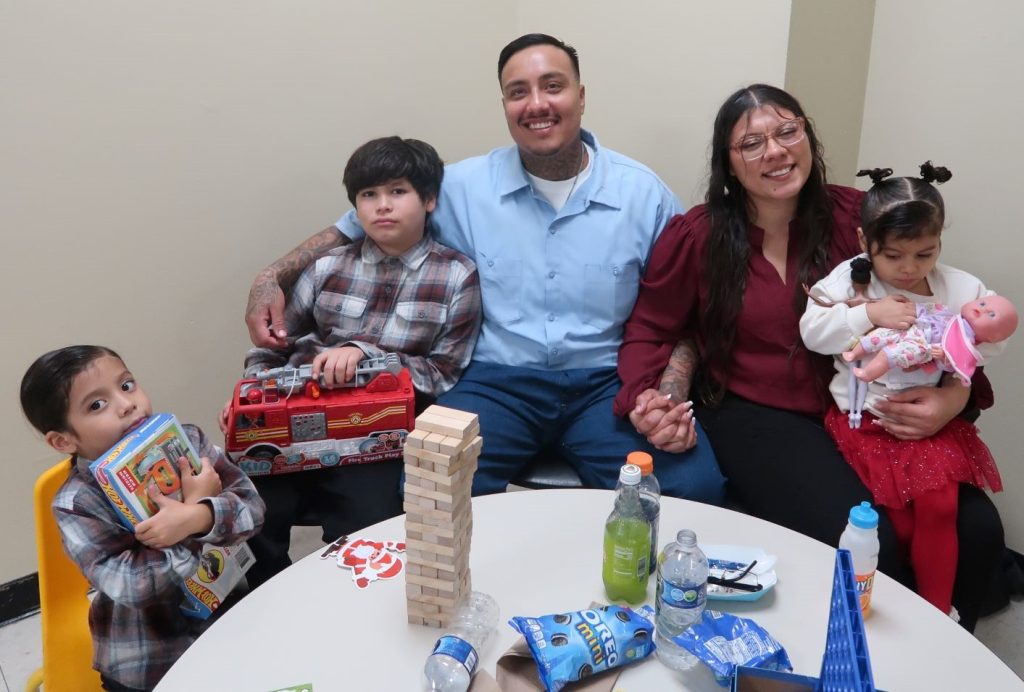 Family smiling with treats, drinks and a game of stacking blocks on a table at Avenal State Prison. 