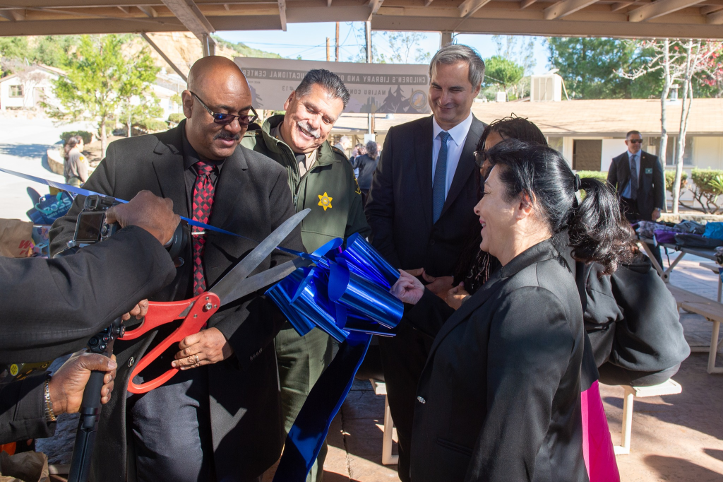 man with giant scissors cutting blue ribbon during ceremony