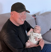 Brian Snider holds a baby. Snider passed away in January 2026.