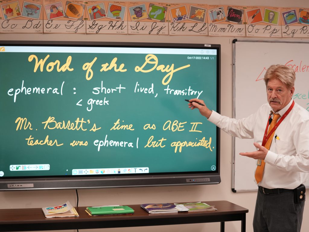 Teacher Brian Barrett, pointing to a screen with a lesson depicted