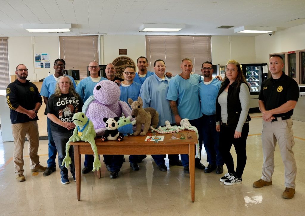 SCC incarcerated persons and staff stand around crocheted and other handmade donation items