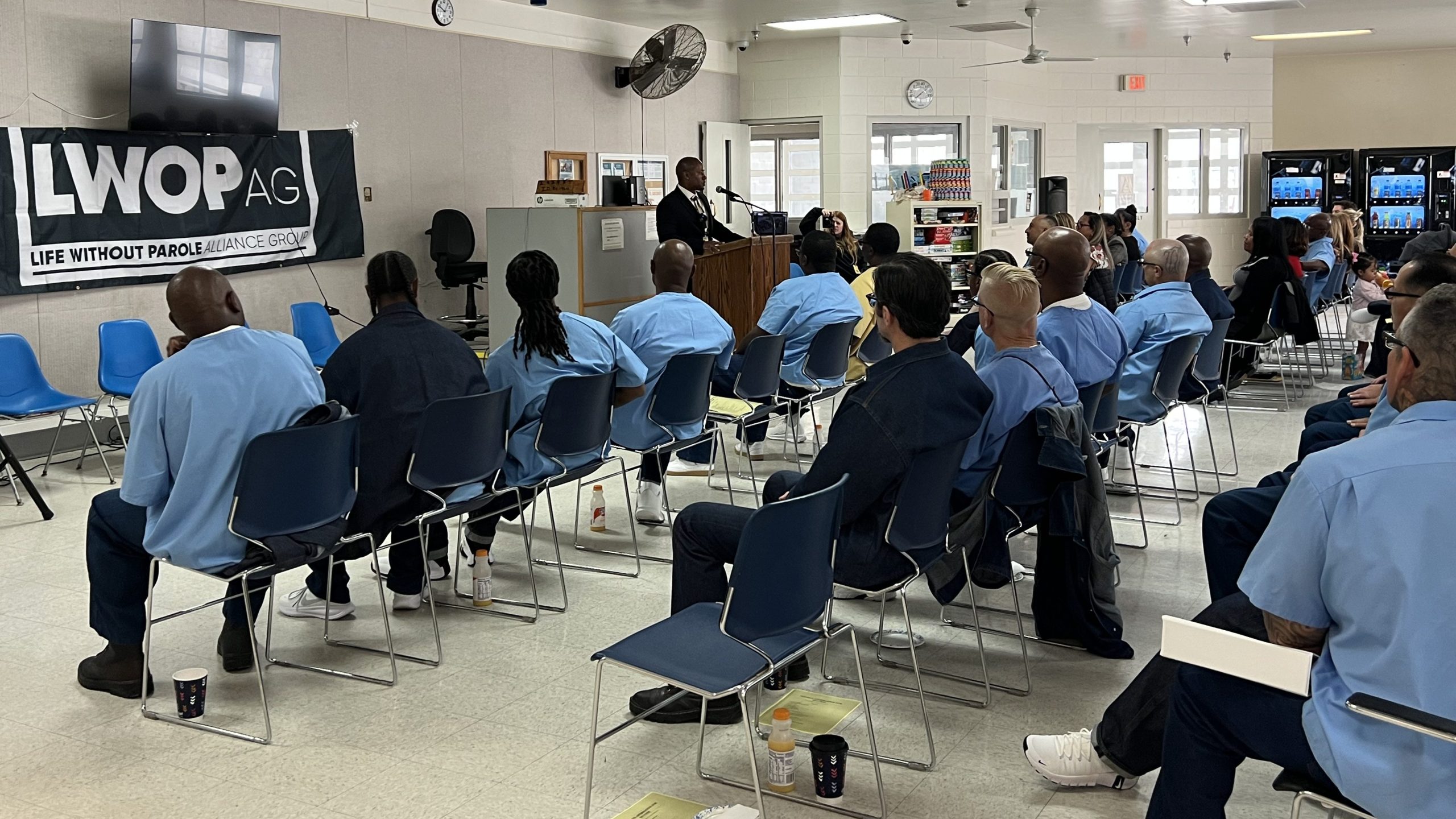 GRADUATES AND ATTENDEES SEATED, LISTENING TO EVENT SPEAKER