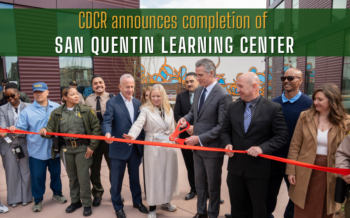 Governor Gavin Newsom stands in a small group as he cuts the ribbon for the San Quentin Learning Center completion event