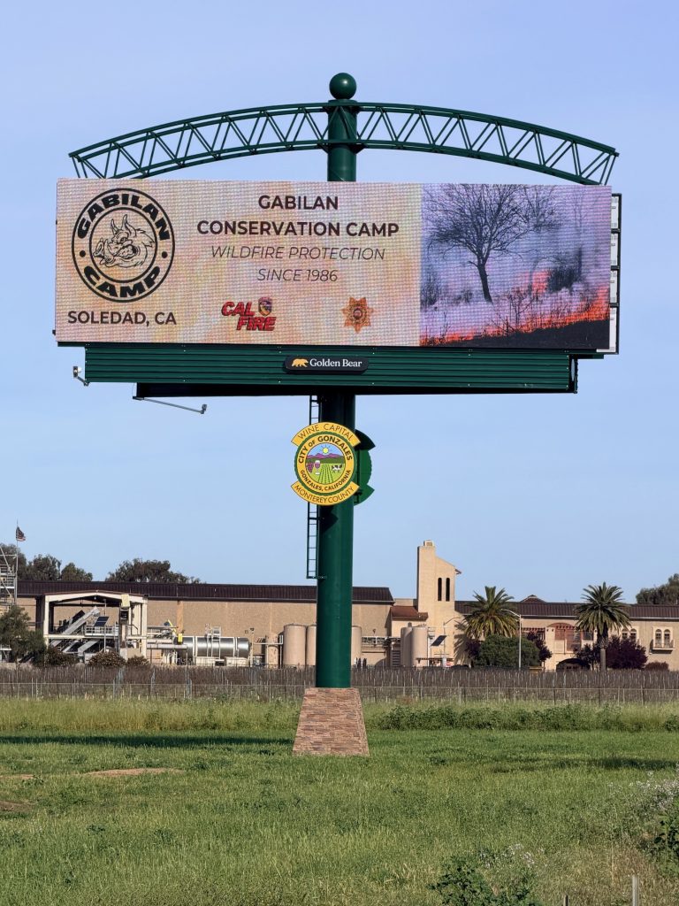 Large billboard with text: Gabilan Conservation Camp, wildfire protection since 1986, Soledad, CA and photo of a grass fire.