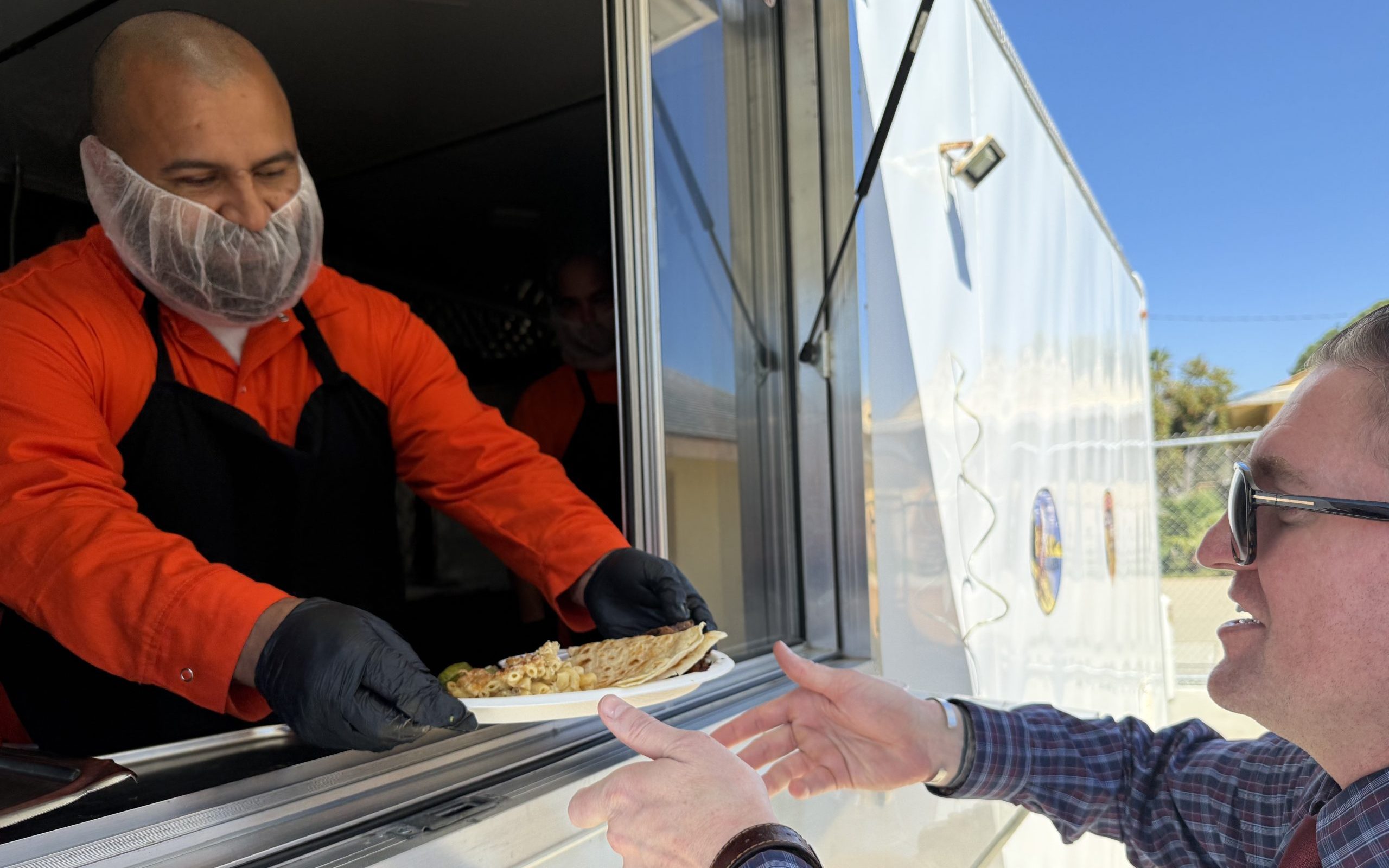 An incarcerated person in the culinary program at CMC hands food to a person waiting in line.