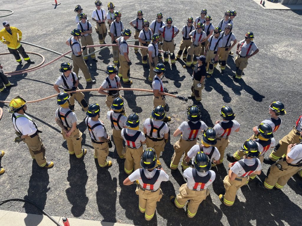 Large group of people in fire uniform holding hoses for training exercise